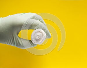 White bandage in a hand in medical glove on bright yellow background.