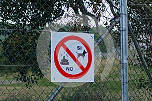 White banner on the netted fence with a red sign - dogs are allowed, pooping is banned