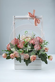 White basket with a bouquet of pink artisanal roses. Pink bow on a wooden handle