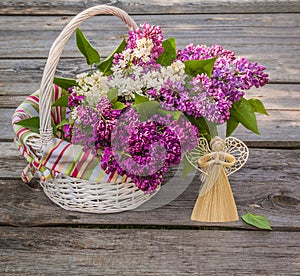 White basket with a branch of lilac and angel made â€‹â€‹of straw