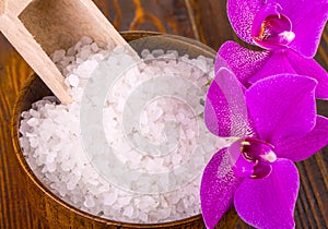 White bath salt and a bag with Orhid on wooden surface.