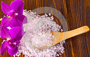 White bath salt and a spoon with Orhid on wooden surface