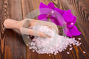 White bath salt and a spoon with Orhid on wooden surface