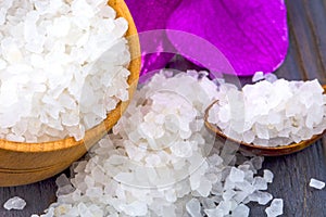 White bath salt in a wooden bowl with a spoon and an orchid