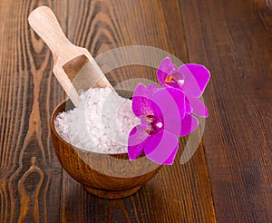 White bath salt in a wooden Cup whith Orhid on wooden surface