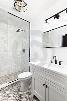 A white bathroom with black and gold light fixtures and tiled floor and shower.