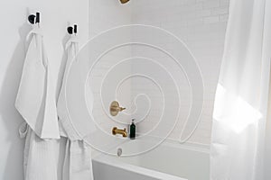 White bathroom shower tub, brass hardware, and bath robes