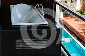 White bathtub at the balcony with pool view below