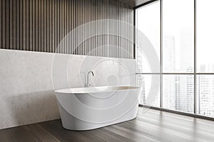 White bathtub on wooden floor in bathroom near window, white wooden design