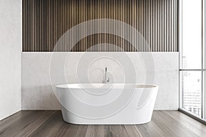 White bathtub on wooden floor in bathroom near window, white wooden design