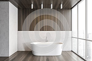 White bathtub on wooden floor in bathroom near window, white wooden design
