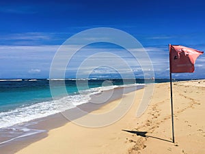 White beach with red flag and perfect blue sea and clear blue sky