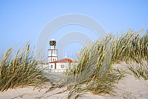 White beach sand dunes and sea oats with Costa Nova church blurred in the background.