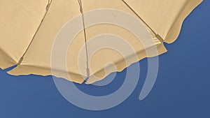 White beach umbrella. Blue sky in the background. View from below. Relaxing context. Summer holidays by the sea