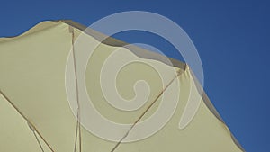White beach umbrella. Blue sky in the background. View from below. Relaxing context. Summer holidays by the sea