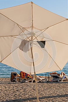 White beach umbrella on summer coast. Sea beach with sun umbrella is waiting for tourists on Sunset.