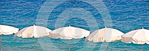 White beach umbrellas aligned on sea background, panoramic summer and tourism concept