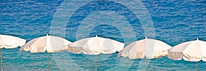 White beach umbrellas aligned on sea background, summer and tourism concept