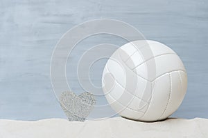 White beach volleyball and heart shape in the sand on grey wooden background
