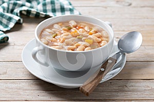 White beans soup with vegetables in white bowl on wood