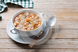 White beans soup with vegetables in white bowl on wooden table