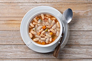 White beans soup with vegetables in white bowl on wooden table