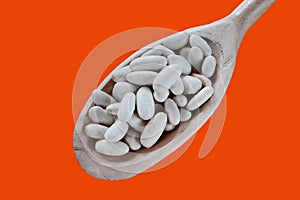 White beans spoon. Closeup of navy beans in a wooden spoon. Orange background