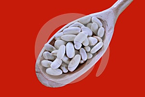 White beans spoon. Closeup of navy beans in a wooden spoon. Red background