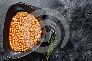 White beans in tomato sauce in a plate. Black background. top view. Copy space