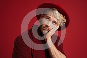 White bearded man wearing hat propping up his head and looking aside