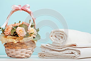 White bed linen sheets roll towels basket with flowers on the table on a blue background