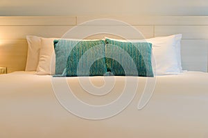 White bed sheets with wooden bedhead in bedroom - stacking of pillows on bed