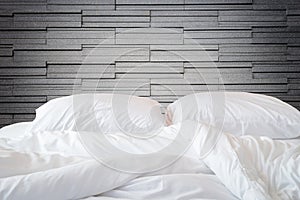 White bedding sheets and pillow on natural stone wall room background, Messy bed concept