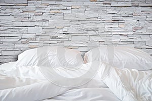 White bedding sheets and pillow on natural stone wall room background, Messy bed concept