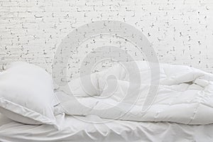 White bedding sheets and pillow in white room background. Messy bed concept in morning time