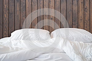 White bedding sheets and pillow on wooden wall room background,