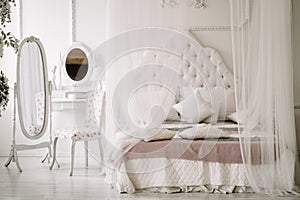 White bedroom interior with nobody. large cozy bed with a white canopy and oval dressing mirror with dressing table next