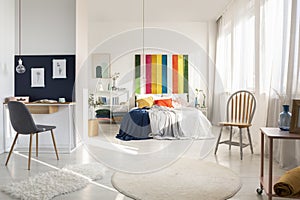 White bedroom interior with workspace with chair and rainbow colored bedhead