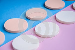 White and beige makeup cosmetic foundation sponges on the blue and pink background, Close up