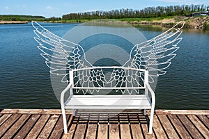 White bench with angel wings on the pier of the blue lake. A place for lovers. Photozone.