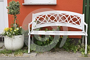 White bench and potted plant in front of a house