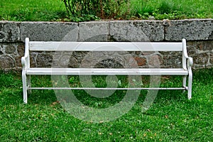 White bench of wood standing on a green lawn