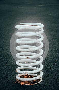 White big, giant spring on a black background. White very large and thick metal spring sticks out of the ground, attached to the