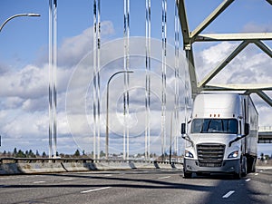 White big rig bonnet semi truck transporting cargo in dry van semi trailer running on the arched bridge with powerful rope bridge