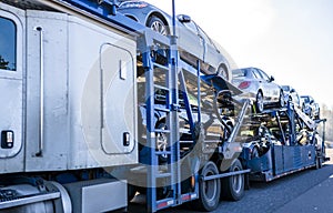 White big rig car hauler long distance semi truck transporting cars on two level semi trailer on the straight road