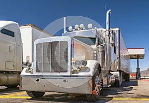 White big rig classic powerful semi truck with chrome accessories and refrigerator semi trailer standing on fuel station in Utah