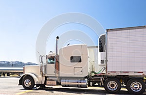 White big rig classic powerful semi truck with refrigerated semi trailer standing on truck stop parking lot in Utah