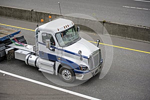 White big rig day cab semi truck with flat bed semi trailer running on the divided highway road