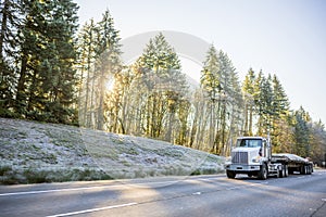 White big rig day cab semi truck for local haul transporting cargo on flat bed semi trailer running on winter road with frost