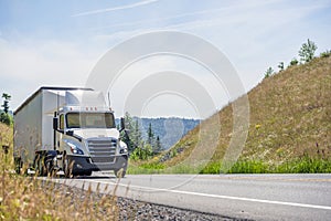 White big rig semi truck with day cab transporting cargo in bulk semi trailer driving uphill in Columbia Gorge